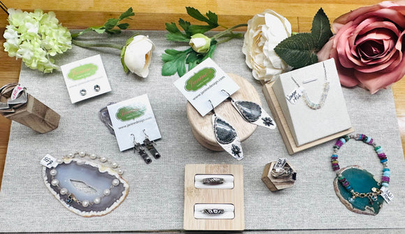assortment of earrings, bracelets and gemstone jewelry on a fabric background with soft pink silk flowers in the background