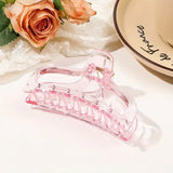 Pink hair clip on a white surface with flowers and a bowl in the background