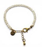 White beaded bracelet with gold clasp and charm on a white background