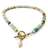 A beaded necklace featuring light blue, green, and beige stone beads with a gold toggle clasp and a dangling white pearl, shown on a plain white background.