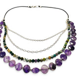 A multi-strand necklace featuring purple amethyst beads, green and brown stone beads, and silver chains on a black cord, displayed on a clean white background.