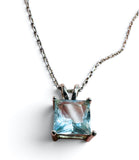 A square-cut light blue gemstone pendant in a silver-toned prong setting on a matching silver chain, shown against a plain white background.