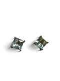 A pair of stud earrings featuring square-cut light blue gemstones in a four-prong setting with dark metal, shown on a plain white background.