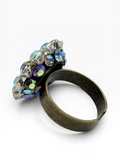 A gothic-style ring featuring a textured, antique bronze band and a cluster of faceted iridescent blue and purple crystals set in a weathered silver-tone metal, shown on a clean white background.