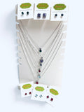 A jewelry display stand holding multiple silver necklaces and several pairs of stud earrings on small branded cards. The necklaces have dark and red gemstone accents, and the earrings are shown both attached to cards and hanging at the top and bottom of the stand.