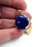 Gold necklace with a blue pendant featuring a starfish held between fingers on a white background. Blue Enamel Locket  Close Up
