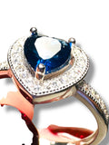 Close-up of a ring with a blue gemstone and diamond accents on a white background. Sapphire Heart Ring