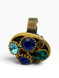 A vintage-style gold ring with a large, rounded cluster of faceted gemstones in blue, green, and light aqua, accented with small purple stones on a white background.