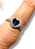 Silver ring with a heart-shaped blue gemstone on a finger against a white background