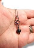 Necklace with a circle design and labradorite bead held in a hand.