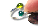 Silver ring with green gemstone held by a finger against a white background