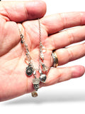 Hand holding a delicate silver necklace with various charms on a white background