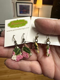 Hand holding floral earrings with a visible brand tag in an indoor setting