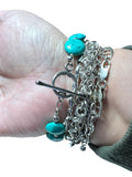 Silver bracelet with turquoise beads on a wrist against a white background