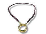 Necklace with purple beads and a gold circular pendant on a white background