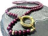 Purple beaded necklace with a gold clasp on a dark surface