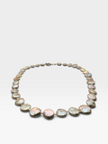 A necklace made of irregular, iridescent shell-like beads in soft pink, green, and cream tones, set in a gold-tone chain, photographed on a light gray background.