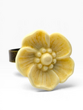 A cream-colored ceramic flower ring with a textured, matte finish and a dark metallic band, shown on a clean white background.