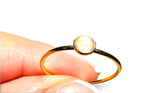 A gold ring with a round, light-reflective stone held between fingers against a white background.