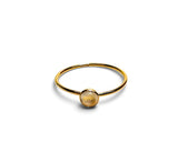A delicate gold ring featuring a smooth, polished round cabochon gemstone in a warm golden-yellow hue, set against a clean white background.