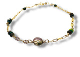 Gold bracelet with green and purple beads on a white background
