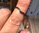 A close-up of a person's finger wearing a thin, wavy black metal band ring, with a jewelry store display visible in the blurred background.