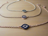 Evil Eye Chain Bracelets crystals shaped into an eye shape attached to chain. shown on wood background