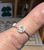 A silver ring with a circular pavé setting featuring a central gold triangle, worn on a finger.