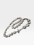 A strand of irregular baroque shell beads with an iridescent, pearlescent finish in shades of gray, silver, and gold, threaded on a dark metal chain with a toggle clasp, photographed on a light gray background.