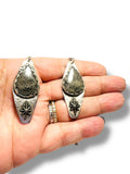 Silver earrings held in a hand on a white background