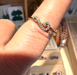 A gold ring with a wavy, openwork design set with small clear crystals, shown worn on a finger in a jewelry display setting.