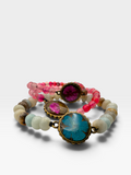 Three beaded bracelets stacked together on a light gray background. The bracelets feature round beads in pink, light blue, cream, and brown, accented by three large oval metal bezel settings containing colorful stone inlays: one magenta, one turquoise, and one pink-brown.