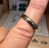 A polished dome-shaped gold ring worn on a finger, with a blurred jewelry display case in the background.