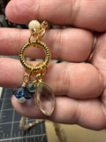 Gold charm with beads held between fingers on a neutral background