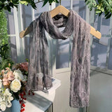 Gray lace scarf on a wooden hanger with flowers and greenery in the background