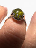 A silver ring with an oval green stone, worn on a finger against a plain white background.