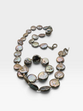 A double-strand necklace made of irregular, polished baroque-style shell beads with an iridescent finish, set in a dark metal with a toggle clasp, photographed on a light gray background.