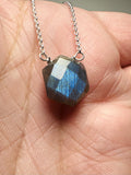 Faceted gemstone pendant on a chain held between fingers