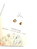 A pair of small gold-toned stud earrings displayed on a cream jewelry card labeled 'June' and 'MOONSTONE' with the words 'WISDOM - SPIRITUAL GROWTH - PASSION' and a geometric watercolor design.