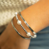 Silver bracelet with pearl beads on a wrist against a blurred background