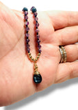 Necklace with beaded chain and blue pendant held in a hand.