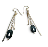 A pair of handmade dangle earrings featuring dark green faceted stone beads with a triangular cutout, suspended from silver-toned chains, textured metal bars, and small silver beads on a plain white background.