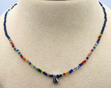 A beaded necklace displayed on a beige jewelry bust. The necklace features small multicolored faceted beads arranged in rainbow-like sections and a polished silver letter 'K' pendant at the center front.