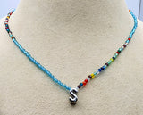 A beaded necklace displayed on a beige jewelry bust. The necklace features a light blue beaded section on each side, transitioning into a strand of small multicolored beads, and ending in a polished silver letter 'S' pendant.