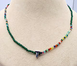 A beaded necklace displayed on a beige jewelry bust. The necklace features dark green beads on the left and right sides, transitioning into a multicolor strand of small faceted beads in the center, with a silver-toned letter 'T' clasp at the front.