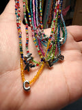 A close-up of a hand holding a bundle of colorful beaded bracelets with silver-toned charms, including one yellow beaded bracelet and several others in red, blue, green, pink, and purple.