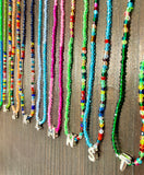 A close-up of multiple colorful beaded necklaces arranged vertically on a dark wood surface, each with a silver letter pendant spelling out the months of the year.