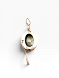 A handmade pendant featuring a round bezel-set labradorite stone in a rose gold-toned metal frame, suspended from a matching rose gold chain with a wrapped bail, shot against a clean white background.
