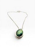 A silver chain necklace with a layered pendant featuring a green and blue labradorite iridescent stone, photographed on a clean white background.