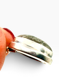 A close-up of a silver ring with a carved labradorite green stone, held between fingers against a plain white background.
